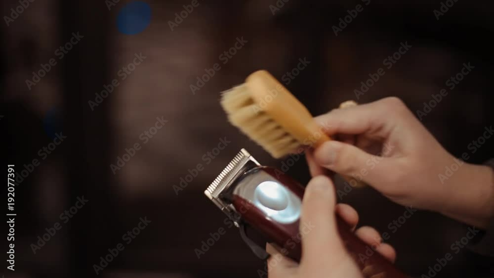 Hairdresser tools. Close up of male hands brushing electric hair clippers. Hairdressers prepare hair machine for next client. Man clean black shaving machine. Hairdresser tools. Close up of male hands brushing electric hair clippers. Hairdressers prepare hair machine for next client. Man clean black shaving machine.