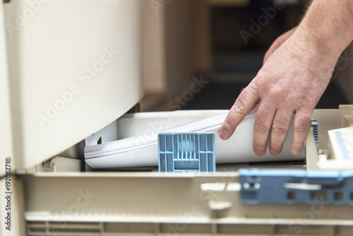 Man's hands placing and ordering blank sheets of paper into paper tray of a photo copying machine