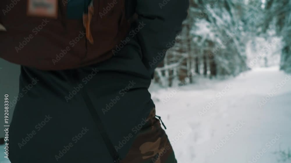 Young man in warm clothes and backpack walking on snow covered pathway in pine woods on cold cloudy winter day, slow motion Young man in warm clothes and backpack walking on snow covered pathway in pine woods on cold cloudy winter day, slow motion