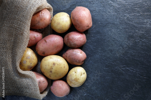 Fotografija Red and Gold potatoes in hessian sack on slate table top with copy space