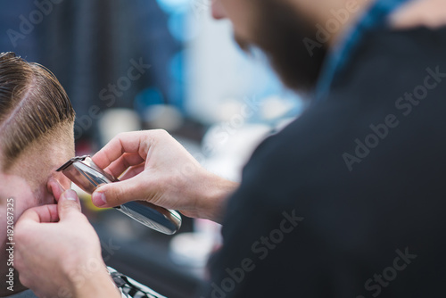 The hairdresser creates a stylish hairstyle for the client. Barber with a beard cutting a young man. Haircut with a hair clipper in the barberchoice