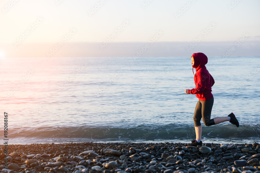 Adult woman runner running on sunrise seaside. Healthy lifestyle.