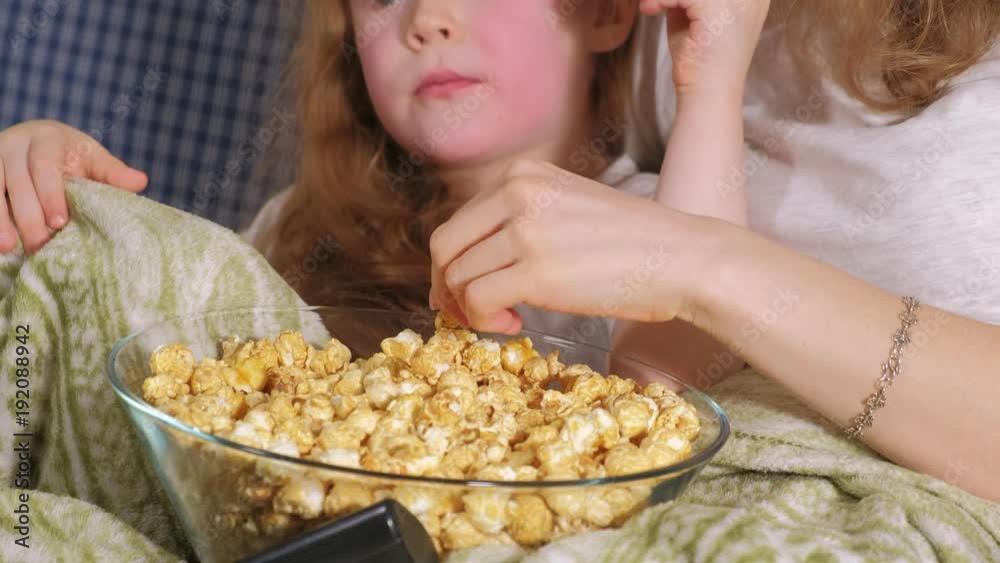 Happy loving family. Mother and her daughter child girl are eating popcorn on the bed in the room. front of the TV Happy loving family. Mother and her daughter child girl are eating popcorn on the bed in the room. front of the TV