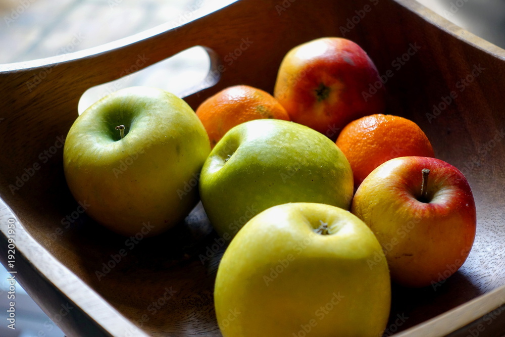 Square wooden fruit bowl containing imperfect red and green apples, and oranges Square wooden fruit bowl containing imperfect red and green apples, and oranges