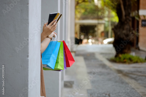 Cropped shot of an unrecognizable woman using her cellphone while standing in front of a building with a bunch of shopping bags
