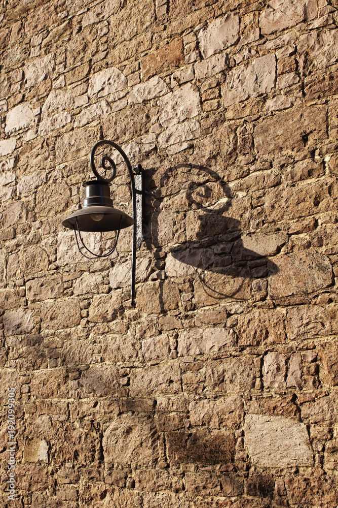 Decorative black street lamp (lantern) and its shadow on historical stone wall in Cunda (Alibey) island.