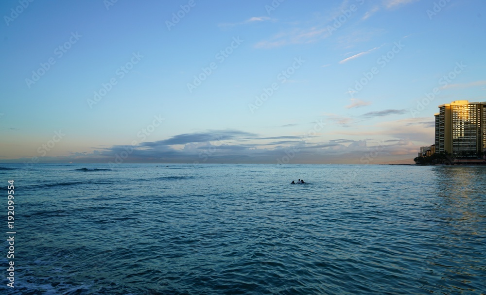 ハワイ　太陽が昇る時刻のワイキキビーチと遠くにサーフィンを楽しむ人たち