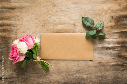  A bouquet of fresh roses and a letter envelope on an aged wooden background. Copy space. View from above.