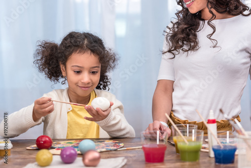 cropped image of african american mother looking how daughter painting easter eggs