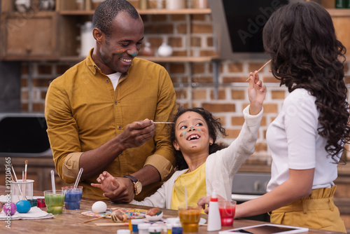Canvas Print happy african american parents and daughter having fun while painting easter egg