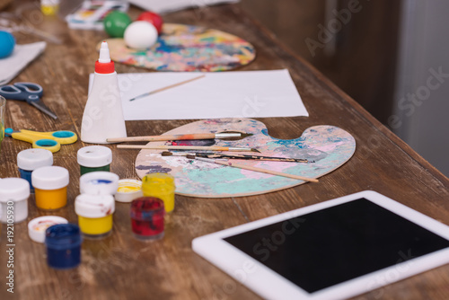 poster paints for easter eggs and tablet on wooden table