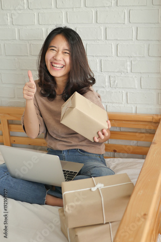 happy laughing joyful accepting woman giving thumg up gesture with computer and product parcel box at home, successful work at home merchandise delivery concept