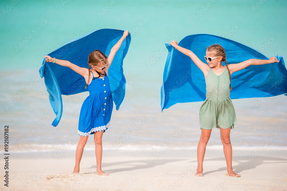 Little girls having fun with towels on tropical beach with white sand and turquoise ocean water