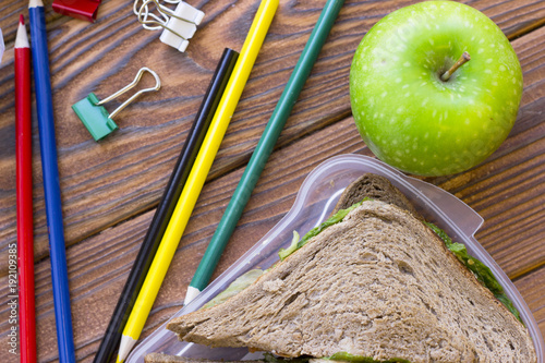 A diet concept. Fresh sandwich with lettuce, an apple, pencils on dark board background