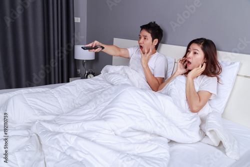 couple watching scared movie with tv remote control on bed