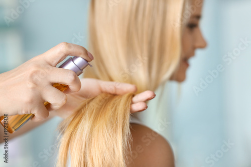 Stylist applying oil onto woman's hair, indoors