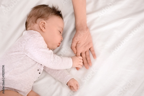 Sleeping baby holding mother's hand on bed