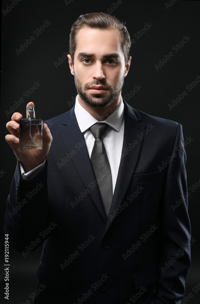 Handsome man in formal suit and with bottle of perfume on dark background Handsome man in formal suit and with bottle of perfume on dark background