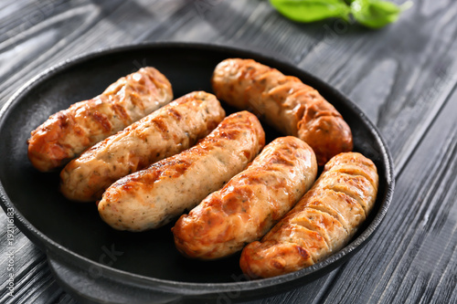 Frying pan with delicious grilled sausages on table