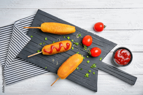 Tasty corn dogs with ketchup on wooden board