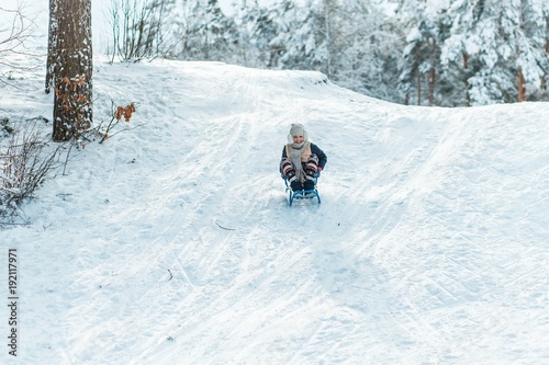 A girl riding sledge down the hill. Beautiful teenage girl having fun outside in a wood with snow in winter on a wonderful frosty sunny day. active life consept