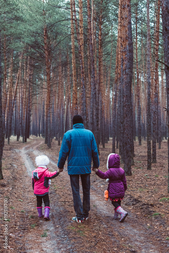 Father and two children walking along the road in a pine forest