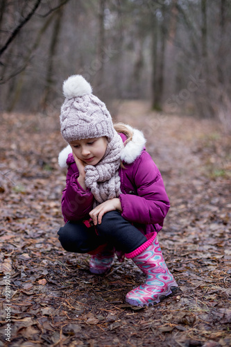 Little cute girl is sitting on the path in the autumn forest.