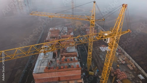 Construction site in the fog with a bird's eye on the Sunset. Aerial Video . Tower crane, excavator and sand. Flying over the construction site. The construction of the plant in the city.