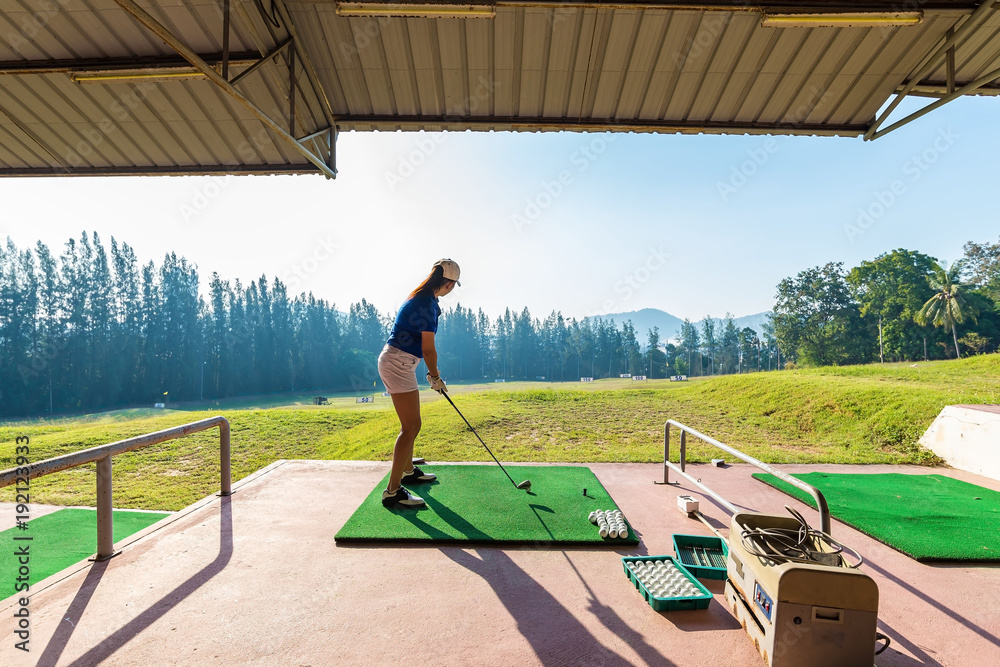 Fototapeta premium Young woman practices her golf swing on driving range, view from behind,Young girls practicing driving range..