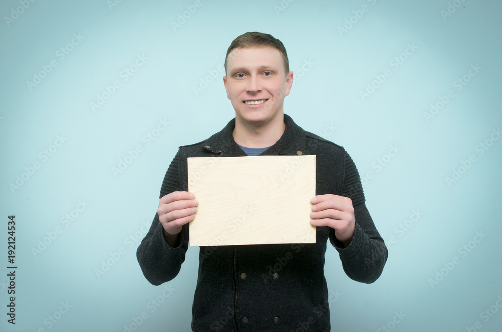 Cheerful young man is holding in hands an empty wooden board with copy space. Billboard. Cheerful young man is holding in hands an empty wooden board with copy space. Billboard.