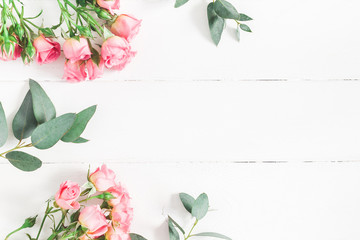 Flowers composition. Frame made of eucalyptus branches and pink rose flowers on white wooden background. Flat lay, top view, copy space