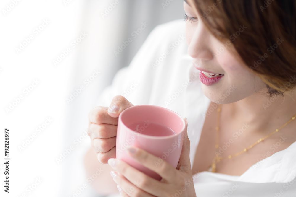 Beautiful woman holding pink cup near window at home. Beautiful woman holding pink cup near window at home.