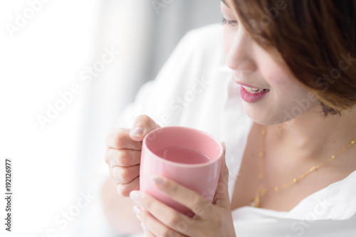 Fototapeta Naklejka Na Ścianę i Meble -  Beautiful woman holding pink cup near window at home.