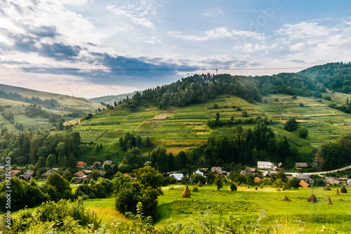 Countryside rural nature landscape in summer sunny day. Discover Ukraine. Village in Carpathians mountains. Beautiful scenic view at green hills and rustic terrain. Farmer houses in forest territory.