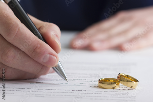 Hands of wife, husband signing decree of divorce, dissolution, canceling marriage, legal separation documents, filing divorce papers or premarital agreement prepared by lawyer. Wedding ring