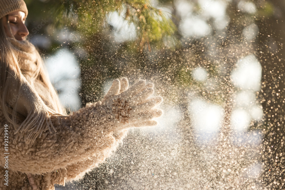Obraz premium Close up of female hands in white knitted gloves, clap and shake hands out of snow at sunny winter day, snowflakes lightened by sun . Winter time concept.