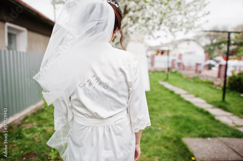 A portrait of a pretty bride posing next to her dress outdoors next to the blossoming tree. © AS Photo Family