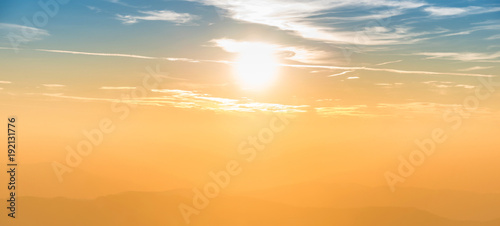 Blue and orange dramatic sky panorama with shining sun and mountains