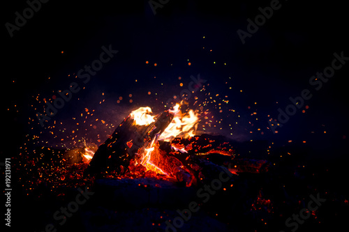 Burning wood at night. Campfire at touristic camp at nature in mountains. Flame amd fire sparks on dark abstract background. Cooking barbecue outdoor. Hellish fire element. Fuel  power and energy.