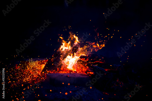 Burning wood at night. Campfire at touristic camp at nature in mountains. Flame amd fire sparks on dark abstract background. Cooking barbecue outdoor. Hellish fire element. Fuel, power and energy. © benevolente