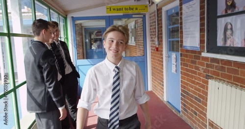 4K Popular & confident young schoolboy walking through school hallway & greeting other pupils. Slow motion