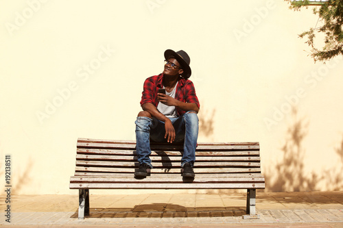 cool african guy in hat sitting on bench by the street