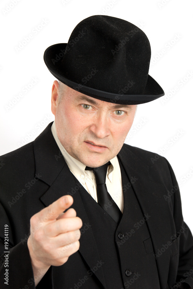 An elderly man in a black suit and black hat accuses someone and points a finger at him. Concept assuse An elderly man in a black suit and black hat accuses someone and points a finger at him. Concept assuse