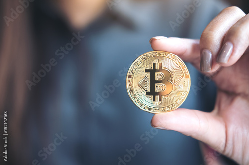 Closeup image of a business woman holding and showing a golden color bitcoin in office
