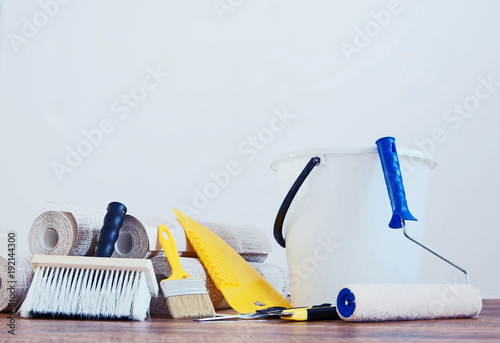 Composition with various tools for wallpapering and rolls of wallpaper against white empty wall