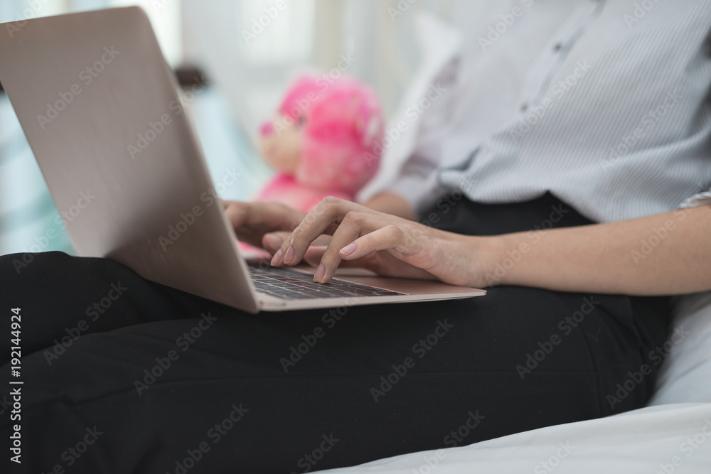 Naklejka premium Hands of Asian business girl while working with a laptop on bed at home.