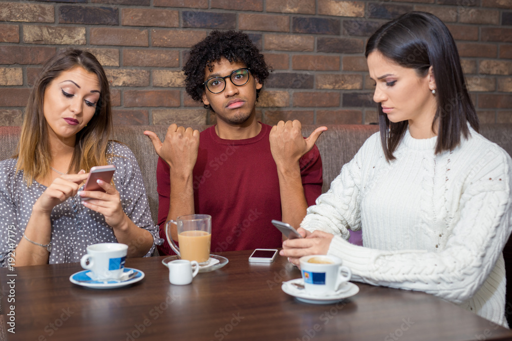 Handsome young man annoyed by two friends playing with their phone Handsome young man annoyed by two friends playing with their phone
