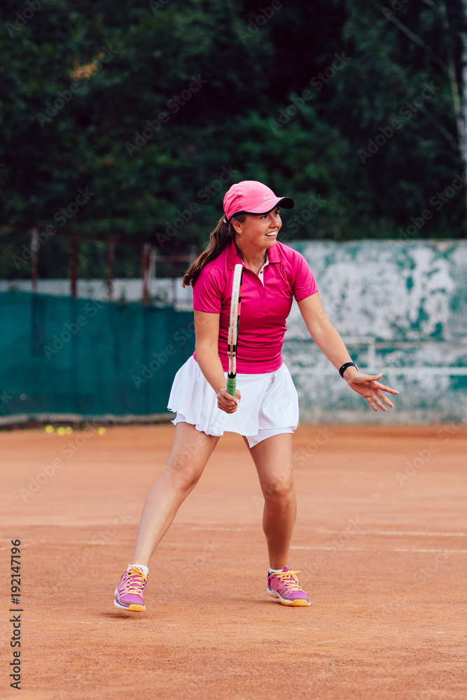 Tennis player. Full length photo of beautiful young woman playing tennis, waiting to receive serve. Dressed in colorful sportswear.