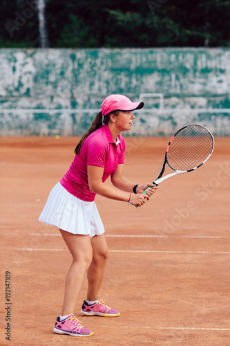 Tennis player. Profile picture of young professional sportive woman in pink t-shirt and white skirt, playing tennis, waiting for the serve. Full length. © Maksym Azovtsev