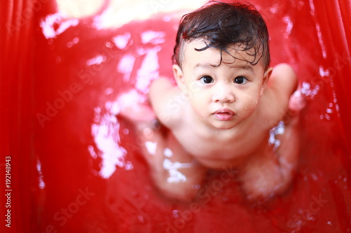 A little asian boy bathes in red inflatable pool in the open air